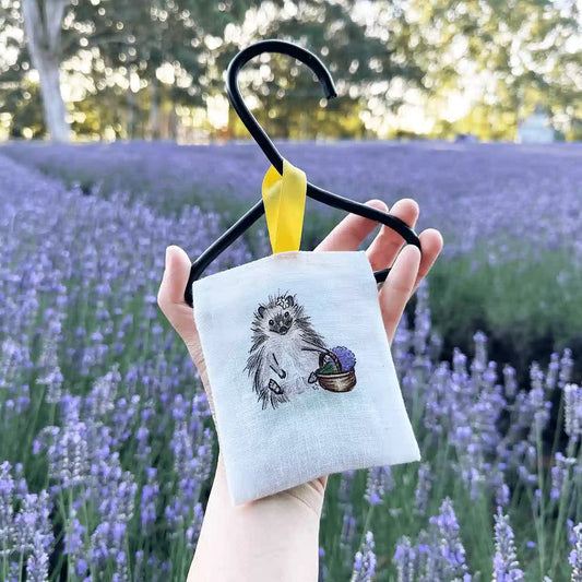 Farm animal hedgehog linen scented sachets designed in NZ for wardrobe and closet to keep moths away, holding by hand against blooming lavender at NZ Lavender Farm.