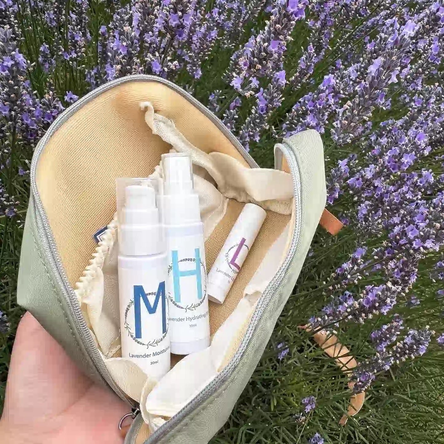 Lavender-Travel-Toiletries-Skincare-Kit, featuring a Travel-Sized Lavender Face Toner, Travel-Sized Moisturiser Lotion, Travel-Sized Lavender Lip Balm, and an Earthy Green Toiletry Bag, displayed among lavender flowers at Lavender Backyard Garden, NZ.