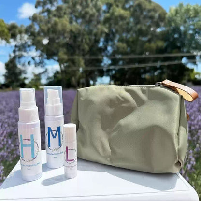 Lavender Travel Toiletries Skincare Kit, featuring a Travel-Sized Lavender Face Toner, Travel-Sized Moisturiser Lotion, Travel-Sized Lavender Lip Balm, and an Earthy Green Toiletry Bag, displayed among a lavender field with white roses in the background.