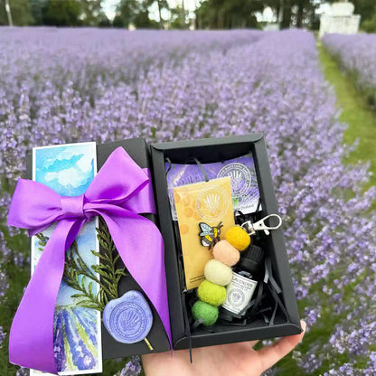 Missing You Sweet Surprise Gift Set scented by lavender essential oils, held by hand against rows of lavender flower bloomings at Lavender Backyard Garden, NZ, featuring products Aromatherapy Pure Lavender Essential Oils, Pastel Felt Ball Keyring Car Diffuser, Very Cute Bee Badge, and Lavender Field Bookmark.