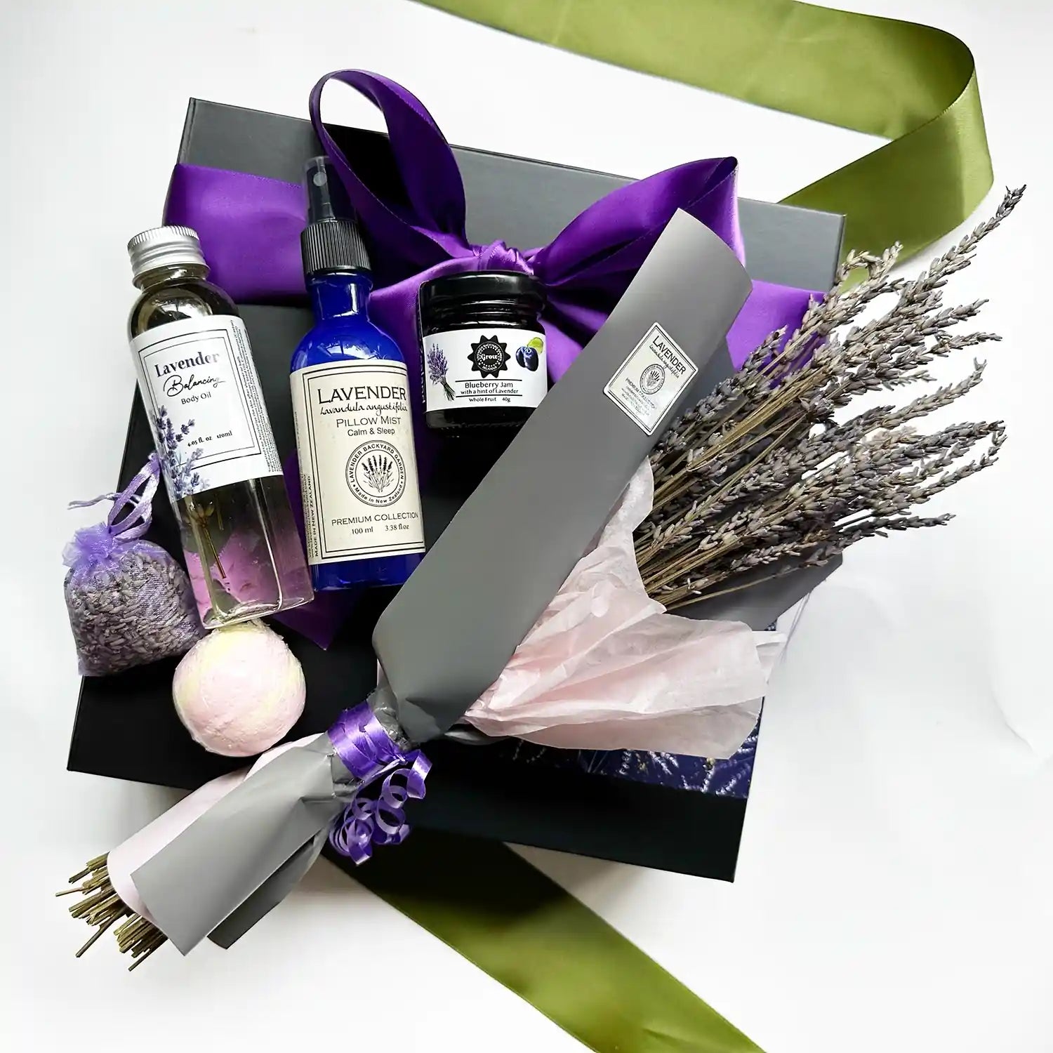 Gift box including a lavender dried flower bouquet, lavender sleep spray, bath bomb, body oil scented by lavender essential oil, and lavender blueberry jam, wrapped with a purple ribbon in a black gift box.