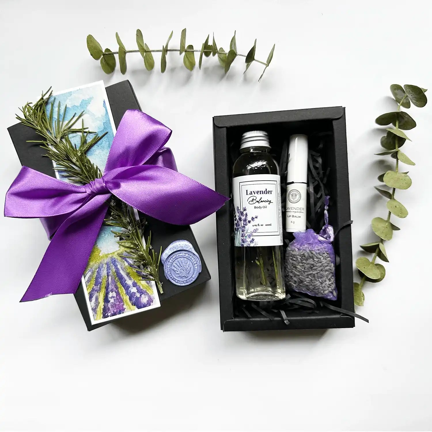 Aromatic Body Care Gift Box featuring lavender body oil, lip balm scented with essential oils, and a lavender sachet, beautifully wrapped in a black gift box with a purple ribbon and a lavender field bookmark.