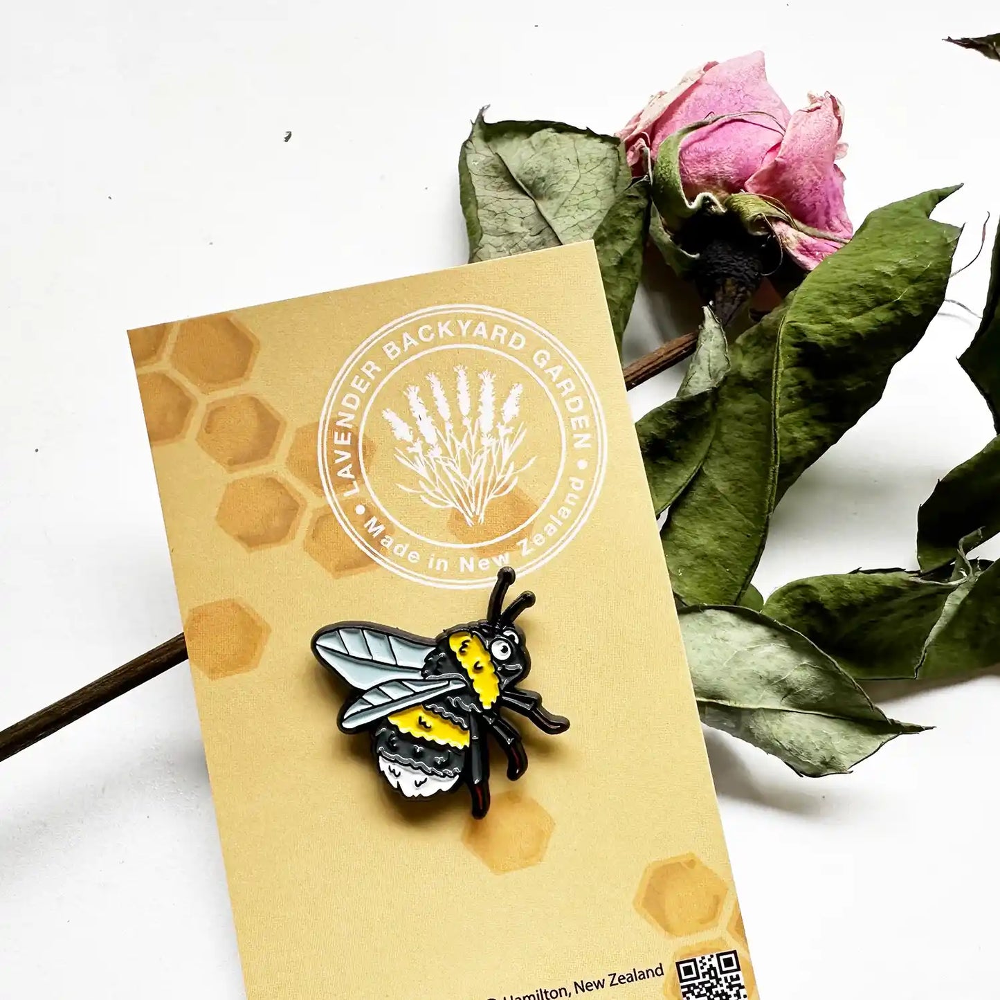 Close-up view of a cute bee enamel pin badge, beautifully contrasted with a dried rose background, capturing the charm of nature and floral elegance.