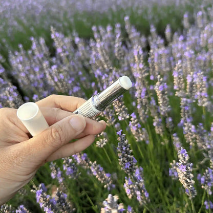 Open lid showing the inner texture of the Lavender Natural Lip Balm for chapped lips, placed against the lavender field at Lavender Backyard Garden, NZ.