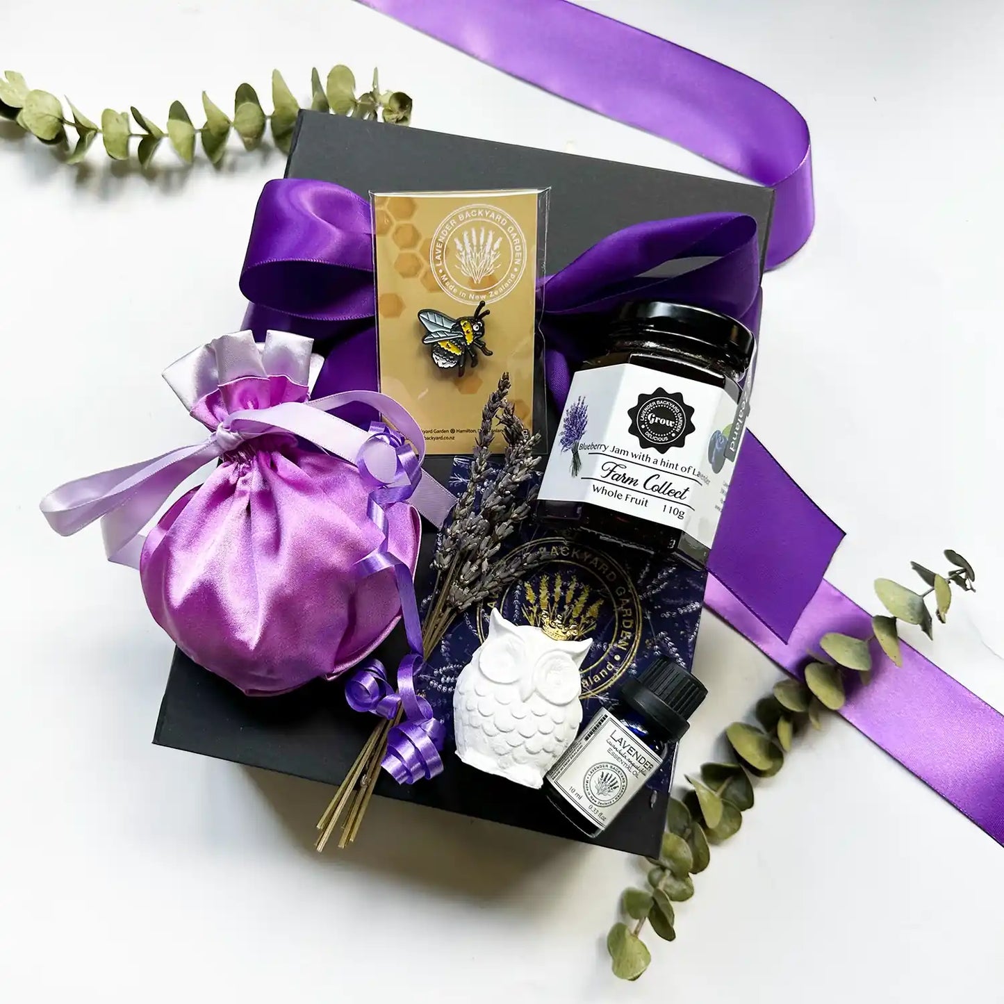 Birthday Harmony Essential Oil Gift Box containing lavender blueberry jam, farm badge, luxury satin lavender bag, mini owl aroma stone, and lavender essential oil, elegantly wrapped in a black gift box with a purple ribbon and mini dried lavender flowers.