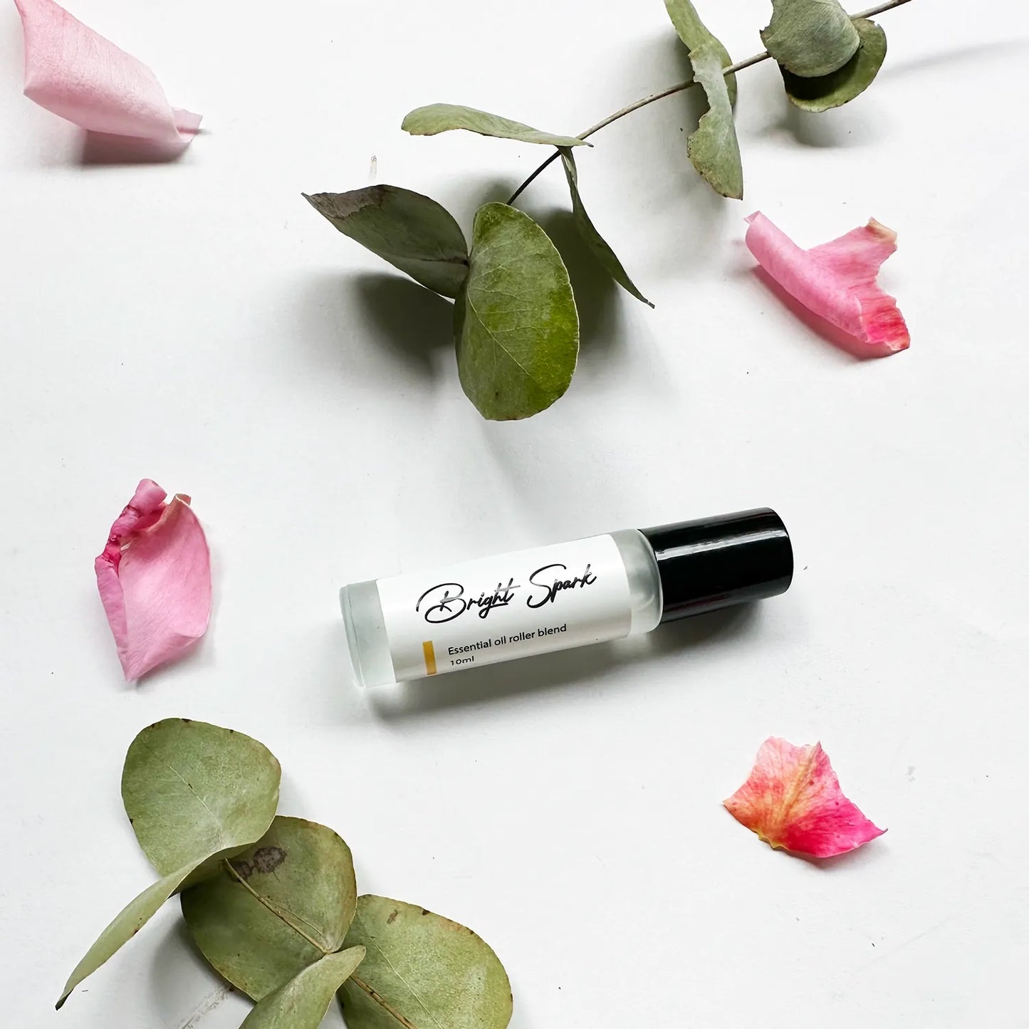 Bright Spark Essential Oil Rollerball - Natural Perfume, surrounded by eucalyptus leaves and pink roses for a fresh, floral display