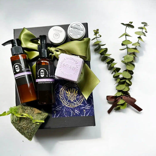 Men’s body oil, body lotion, eucalyptus and lavender sachet, goat milk handmade soap, and lip balm infused with lavender essential oil, arranged with a eucalyptus leaves bouquet in a black gift box with a green ribbon background