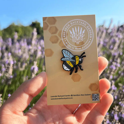 Close-up view of a bee badge designed in New Zealand, set against a backdrop of vibrant lavender blooms and a clear blue sky.