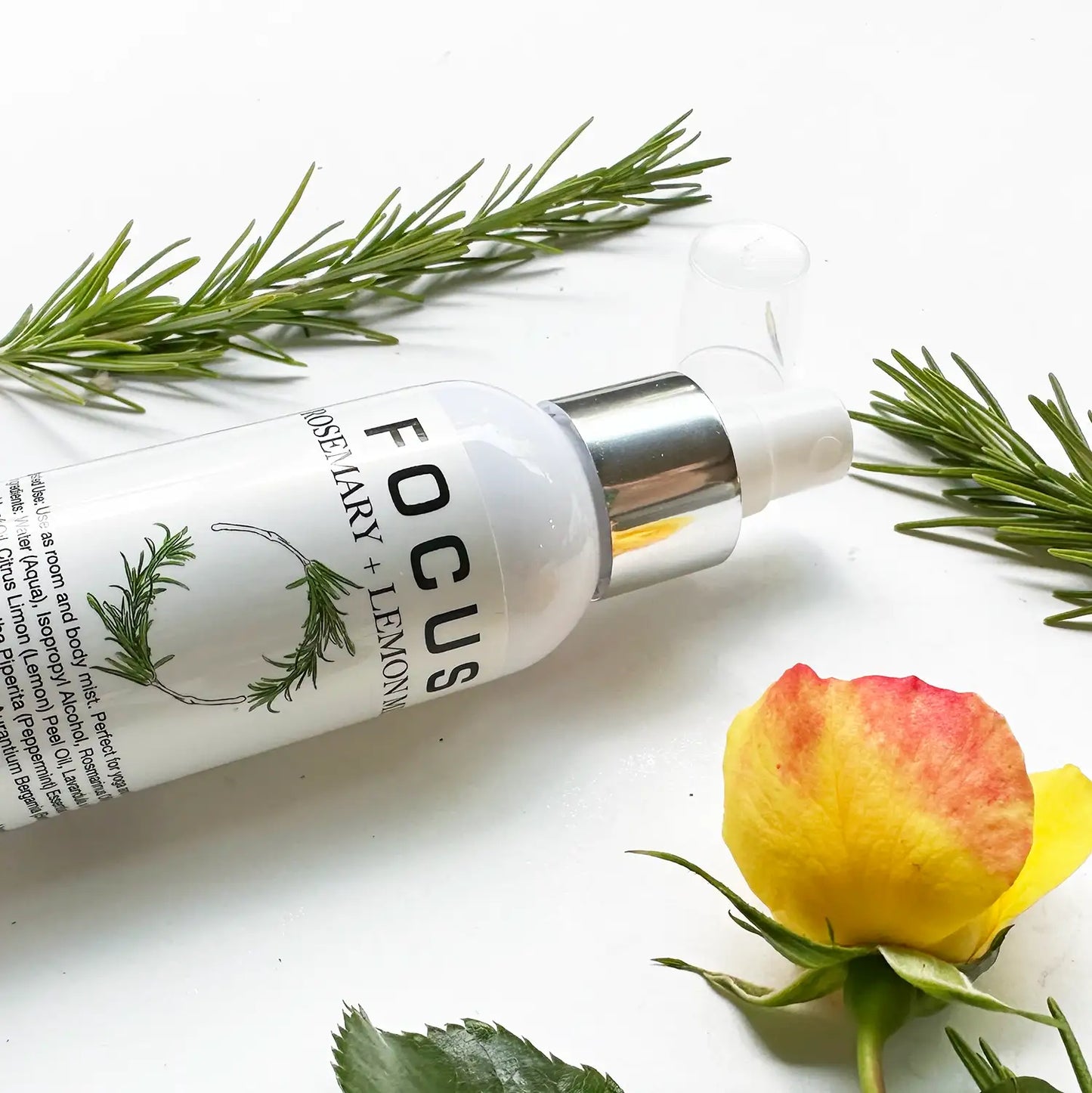 Close-up view of Focus Aromatherapy Spray with Pure Essential Oils, featuring a background of rose flowers and fresh rosemary leaves.