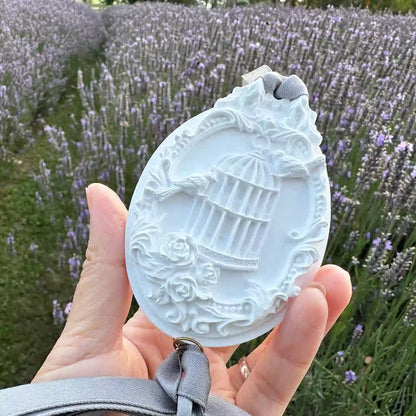 A hand holding a lavender aroma stone diffuser, designed as an air refresher, against the backdrop of a vibrant purple lavender field.