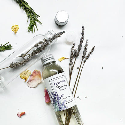 Close-up of lavender essential oil-scented body oil, ideal for dry skin, with an empty bottle, dried lavender flowers, rosemary, and rose petals in the background.