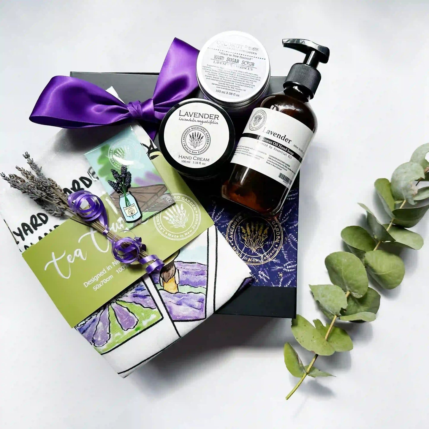 Comforting Kitchen Treats for Mother gift set with lavender-scented hand wash, hand scrub, hand cream, lavender field-themed tea towel, dried lavender, and a fridge magnet, displayed with a purple ribbon gift box in the background.