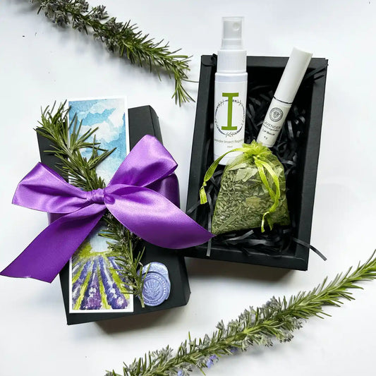 Compact Personal Care Gift Box featuring travel-size insect repellent, lavender-scented lip balm, and lavender eucalyptus sachet, wrapped in a black gift box adorned with a purple ribbon, dried lavender flowers, and a bookmark.