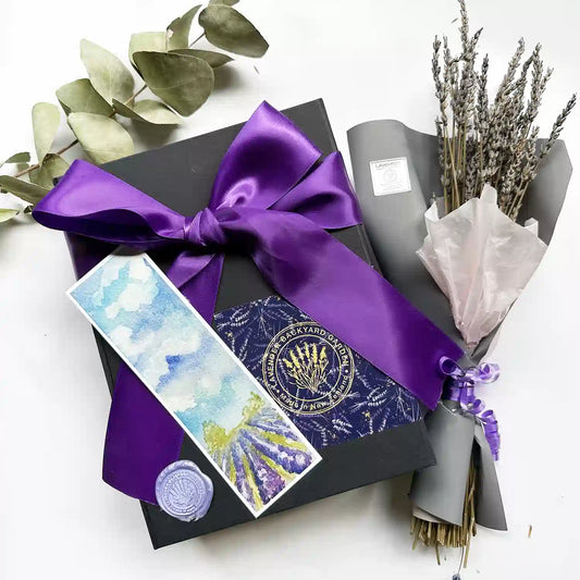 Elegant black gift box tied with a purple ribbon, accompanied by dried lavender flowers and a lavender field bookmark.