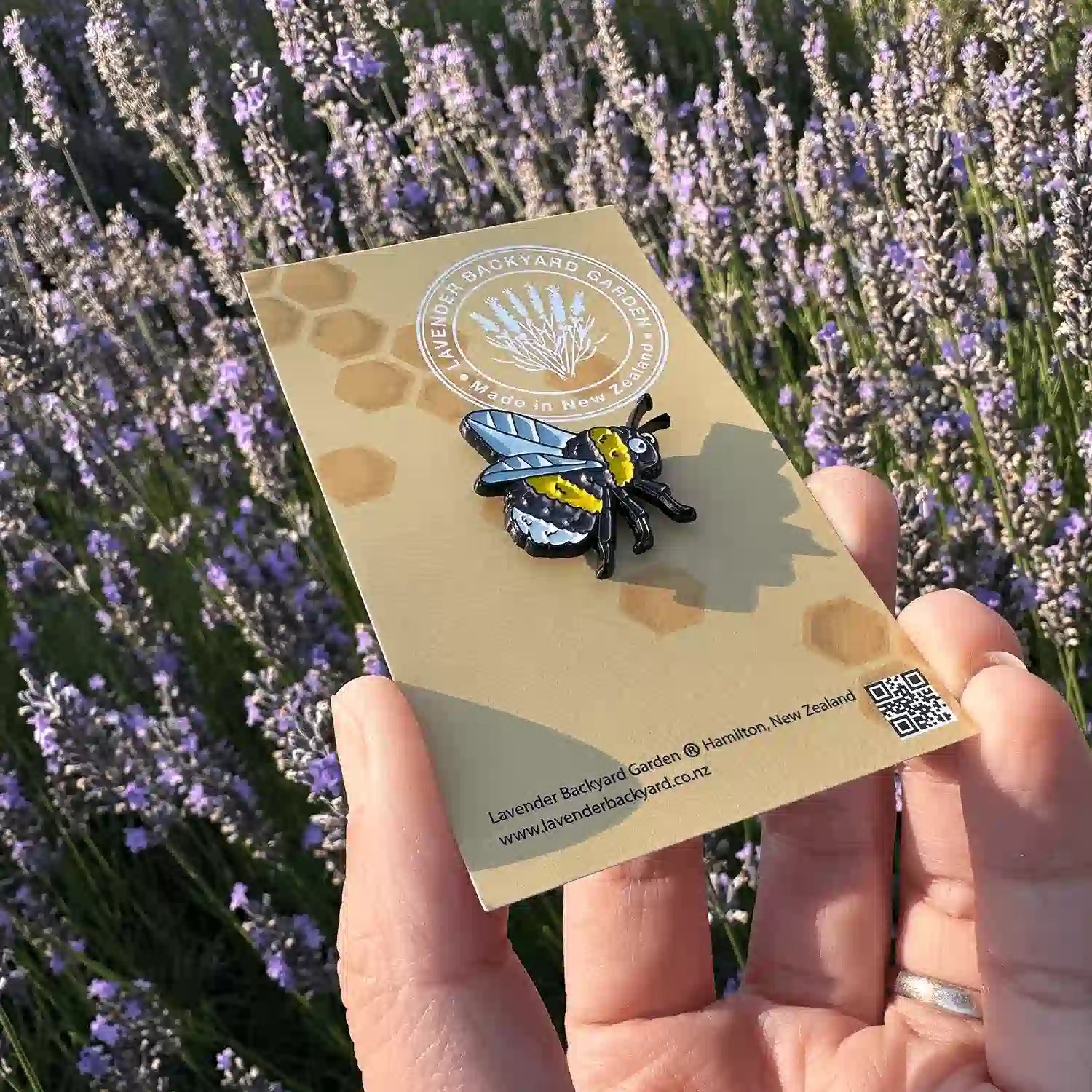 Close-up look of a cute bee badge designed in NZ, set against blooming lavender bushes at Lavender Backyard Garden.