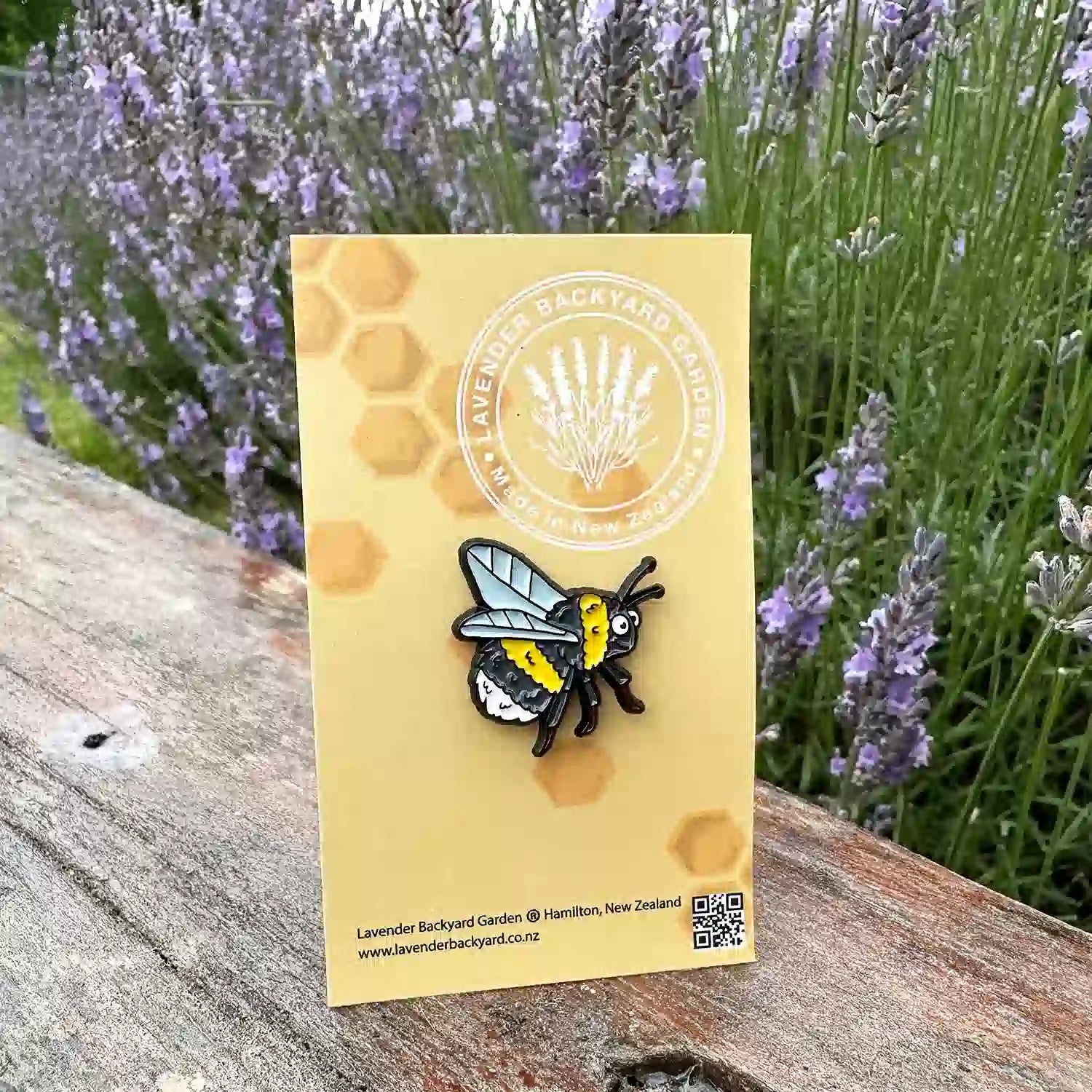 A cute bee enamel badge placed on a wooden bench with a vibrant lavender field in the background, capturing the charm of the badge against the serene setting.