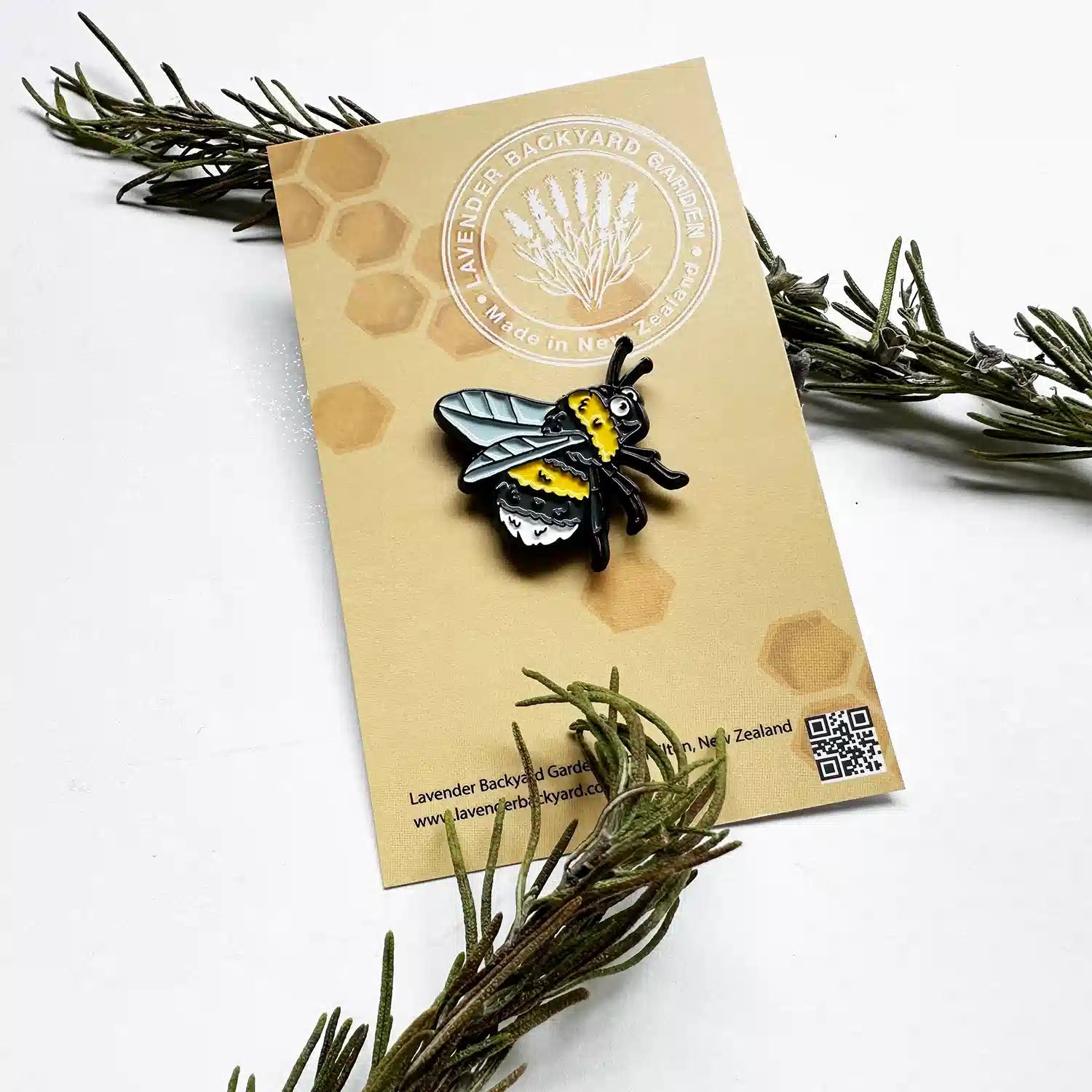 Cute enamel pin badge featuring a bee design, set against a background of fresh rosemary leaves, symbolizing the charm of a lavender farm.