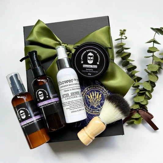 Dad's Premium Grooming Collection featuring lavender body oils for men, lavender men's aftershave refreshing lotion, lavender & mint daily moisturizing after-shower mist, lavender soothing shaving soap, and a classic shaving brush, displayed in a black gift box with a green ribbon background.