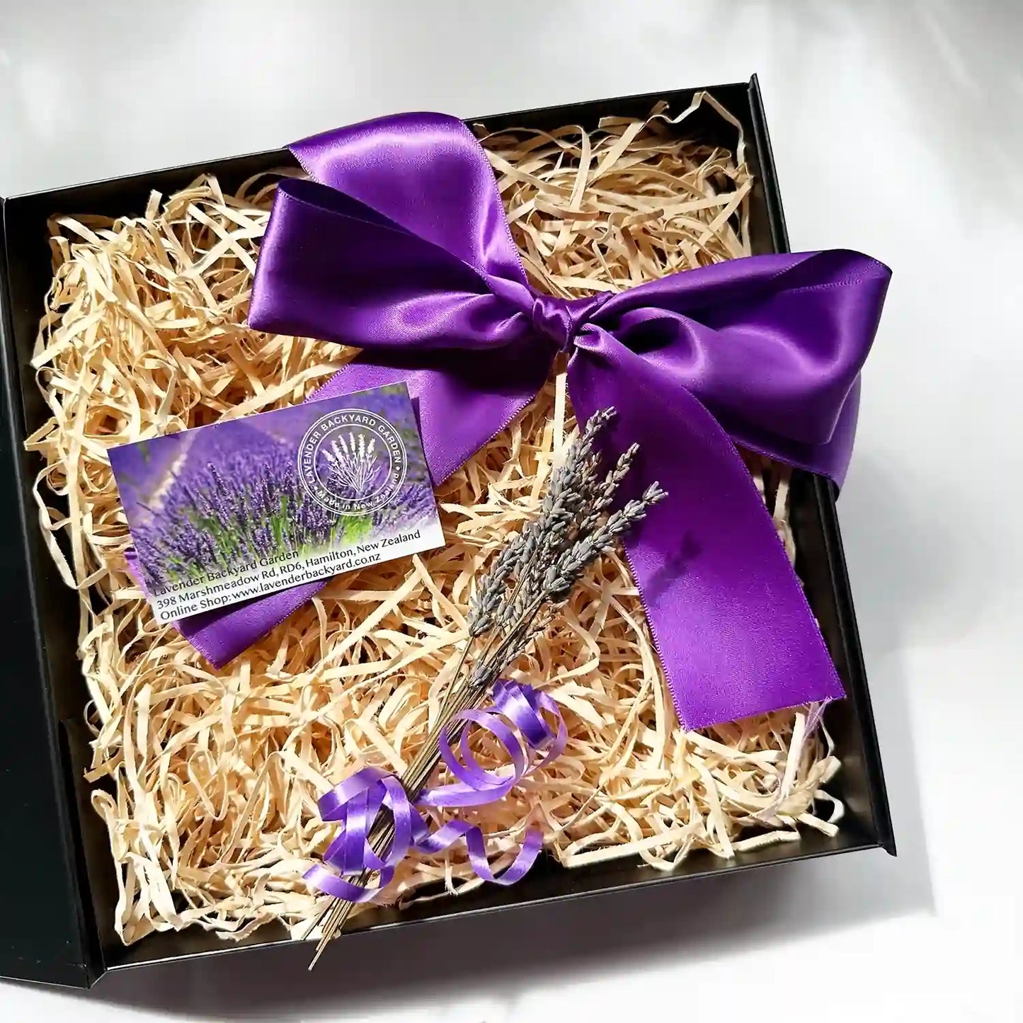 Empty large gift box containing a lavender backyard garden business card, dried lavender flowers, black gift box, and purple ribbon.