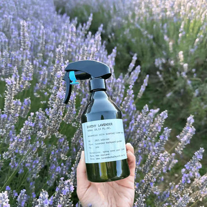 Earthy Lavender & Vetiver Linen Spray bottle held by hand against the backdrop of lush purple lavender fields at Lavender Backyard Garden, NZ.