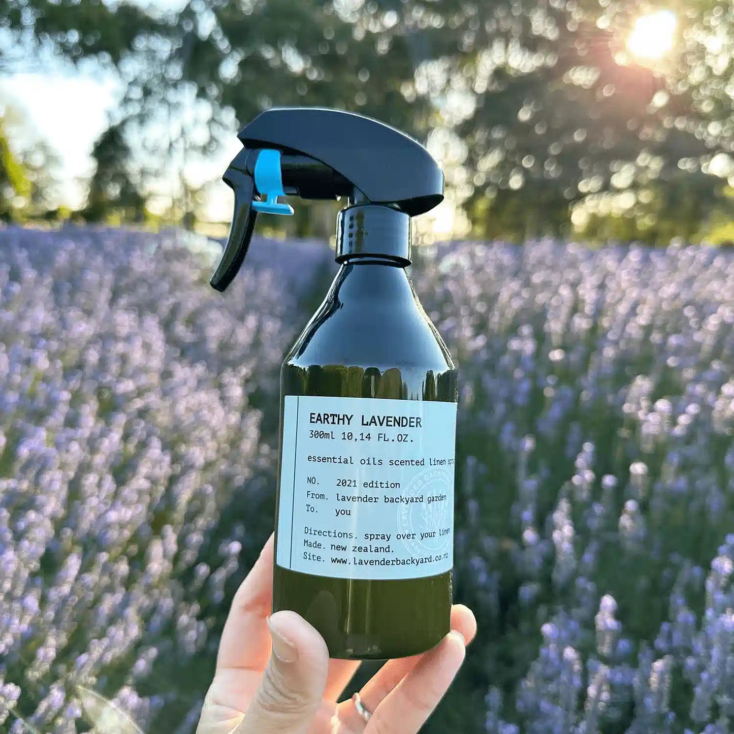 Earthy Lavender Room Spray, holding by hand against purple lavender field at sunset at NZ lavender farm lavender backyard garden.