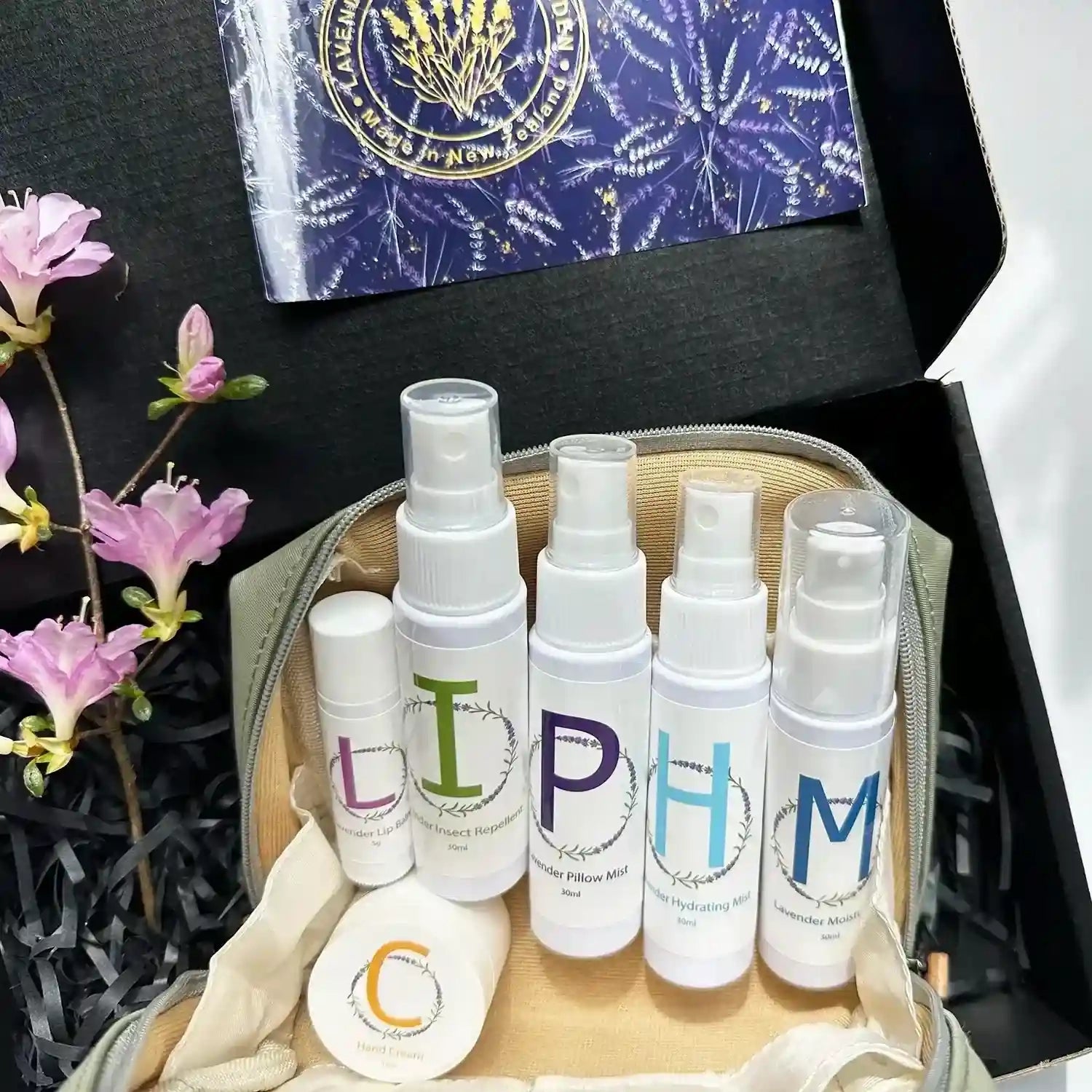 Travel-sized self-care essentials featuring lavender products: pillow mist, face mist, insect repellent, moisturiser lotion, hand cream, and lip balm, all packed in an earthy green toiletry bag.