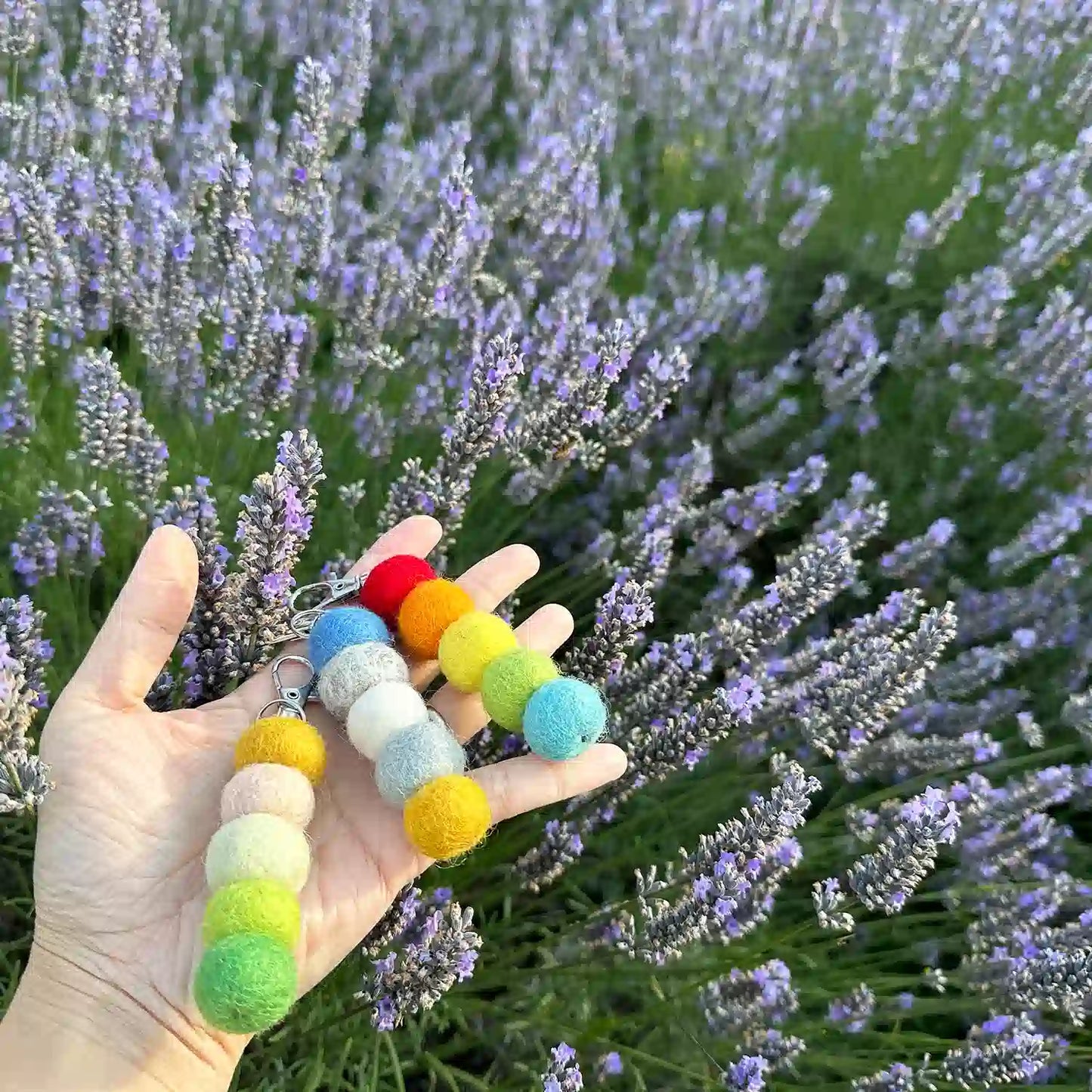 Three colorful felt ball air fresheners held by hand against a backdrop of lavender fields.