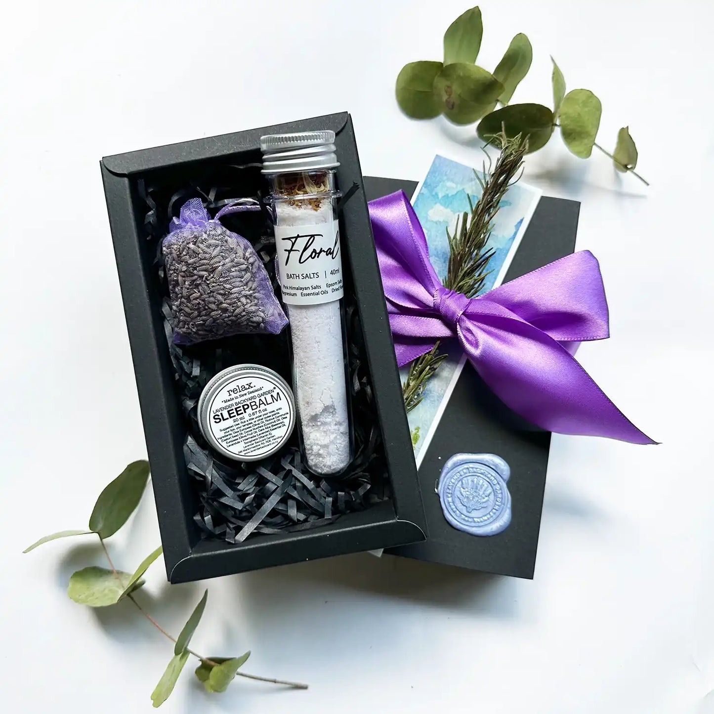 A beautifully arranged gift set featuring lavender sleep balm, bath salt scented with essential oils, and a lavender sachet, all wrapped with a purple ribbon and accompanied by a lavender field bookmark.