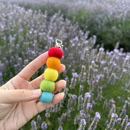 Handcrafted pastel felt ball essential oil air freshener held against a purple field of blooming lavender.