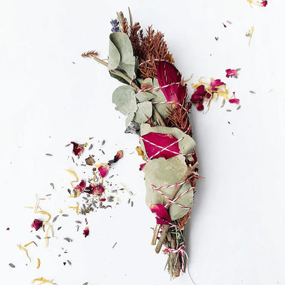 One dried smudge stick containing lavender, cedarwood, white sage, rosemary, eucalyptus, and roses, set against a background of rose petals.