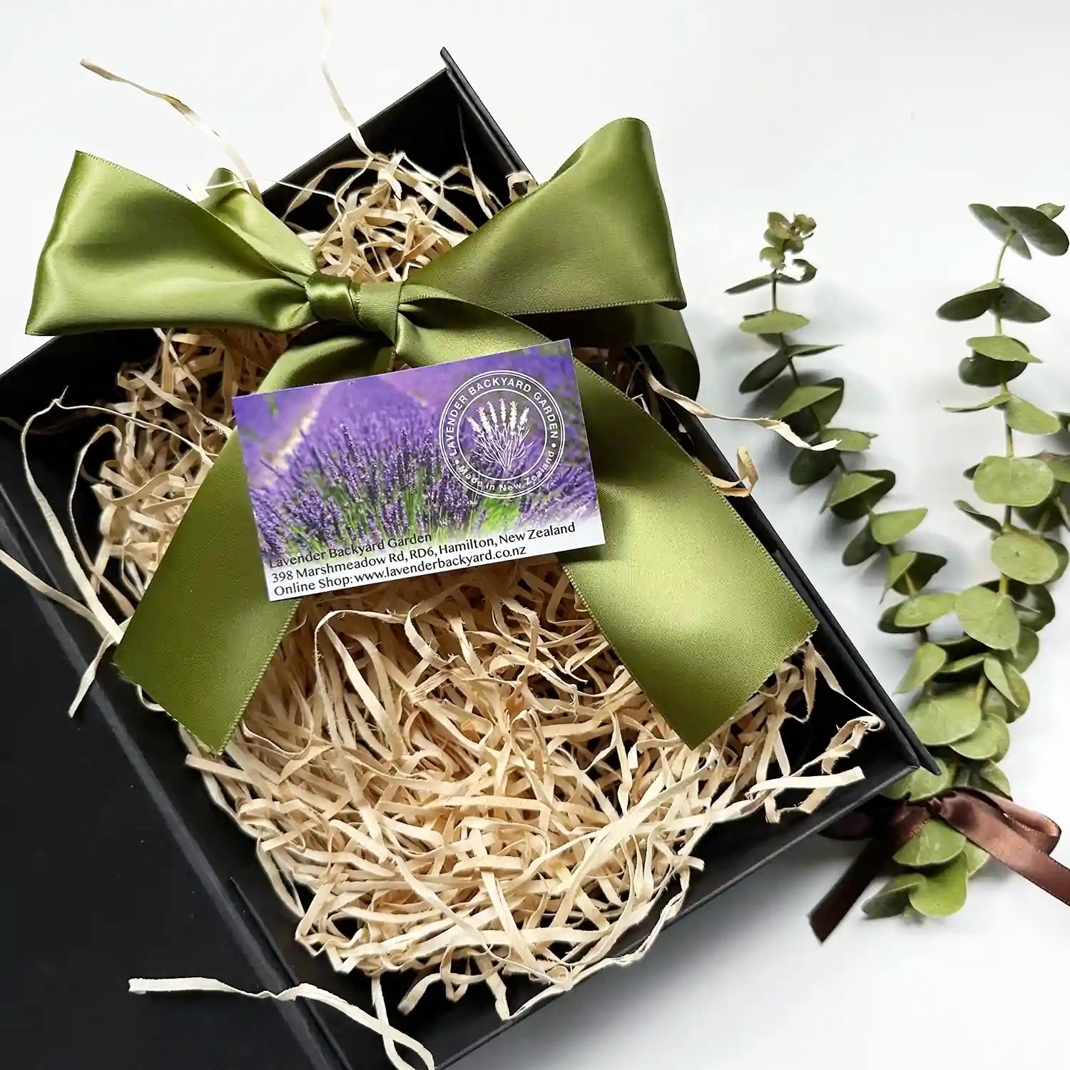 Large empty gift box with green ribbon and eucalyptus bundle in the background for design your own gift set