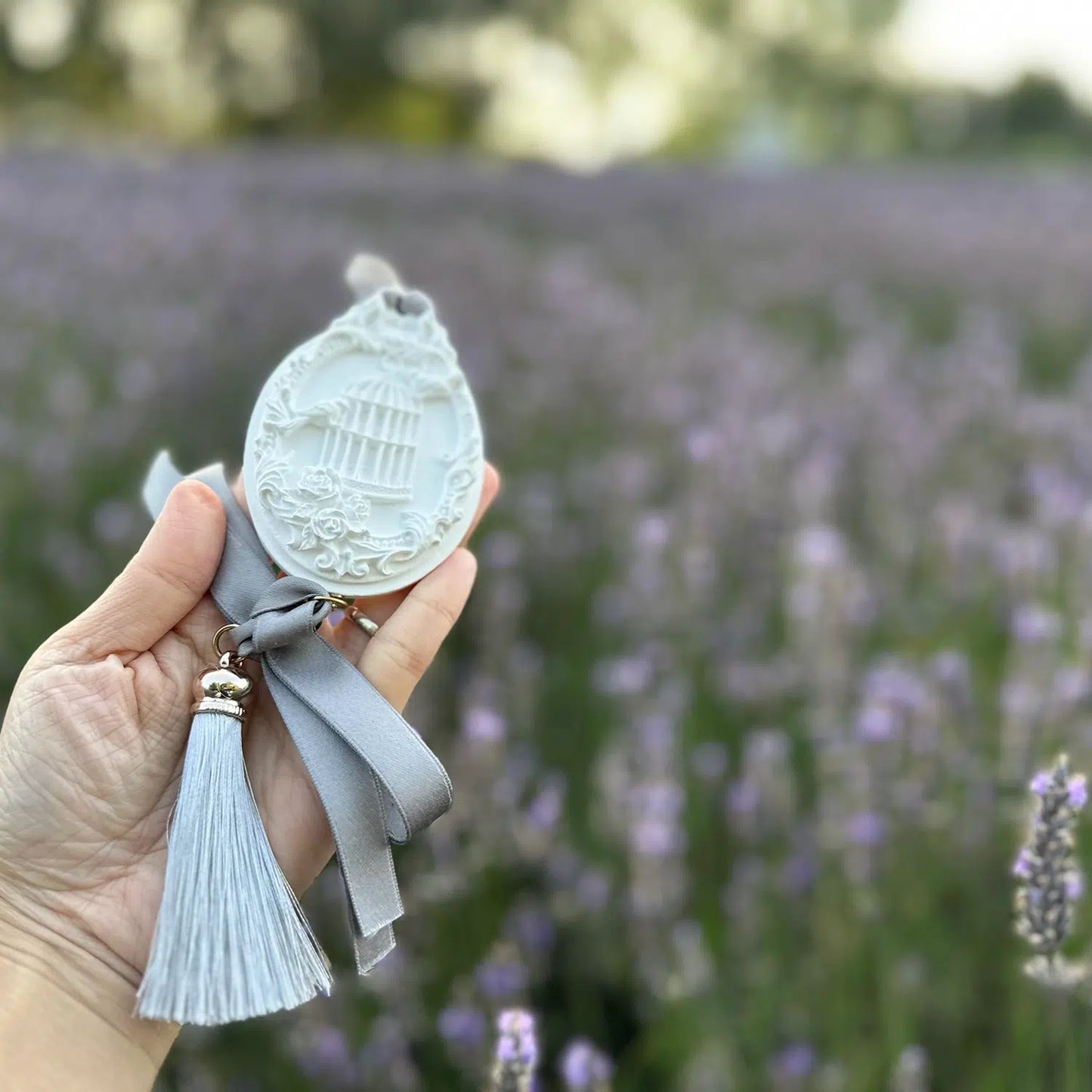 A hand holding a lavender aroma stone diffuser, designed as an air refresher, slightly far away against a vibrant purple lavender field at Lavender Backyard Garden in New Zealand.