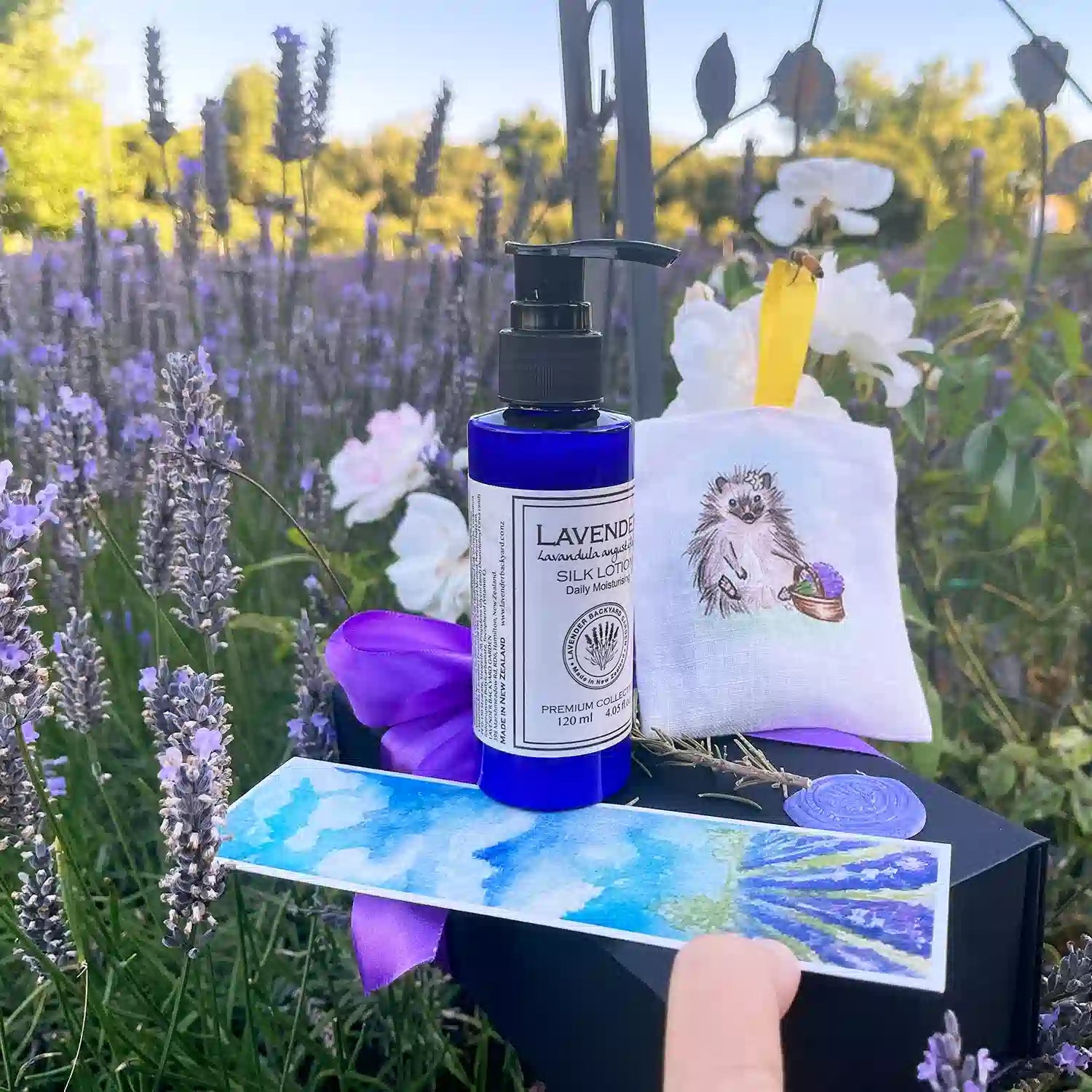 Lavender Dreams: Good Birthday Presents for Girls, featuring a beautiful gift set with Linen Lavender Scented Hanging Sachets-Hedgehog, Moisturizing Lavender Body Lotion, Lavender Field Bookmark, and Mini Lavender Dried Flowers, set against a sunset lavender field and white roses at Lavender Backyard Garden, NZ.