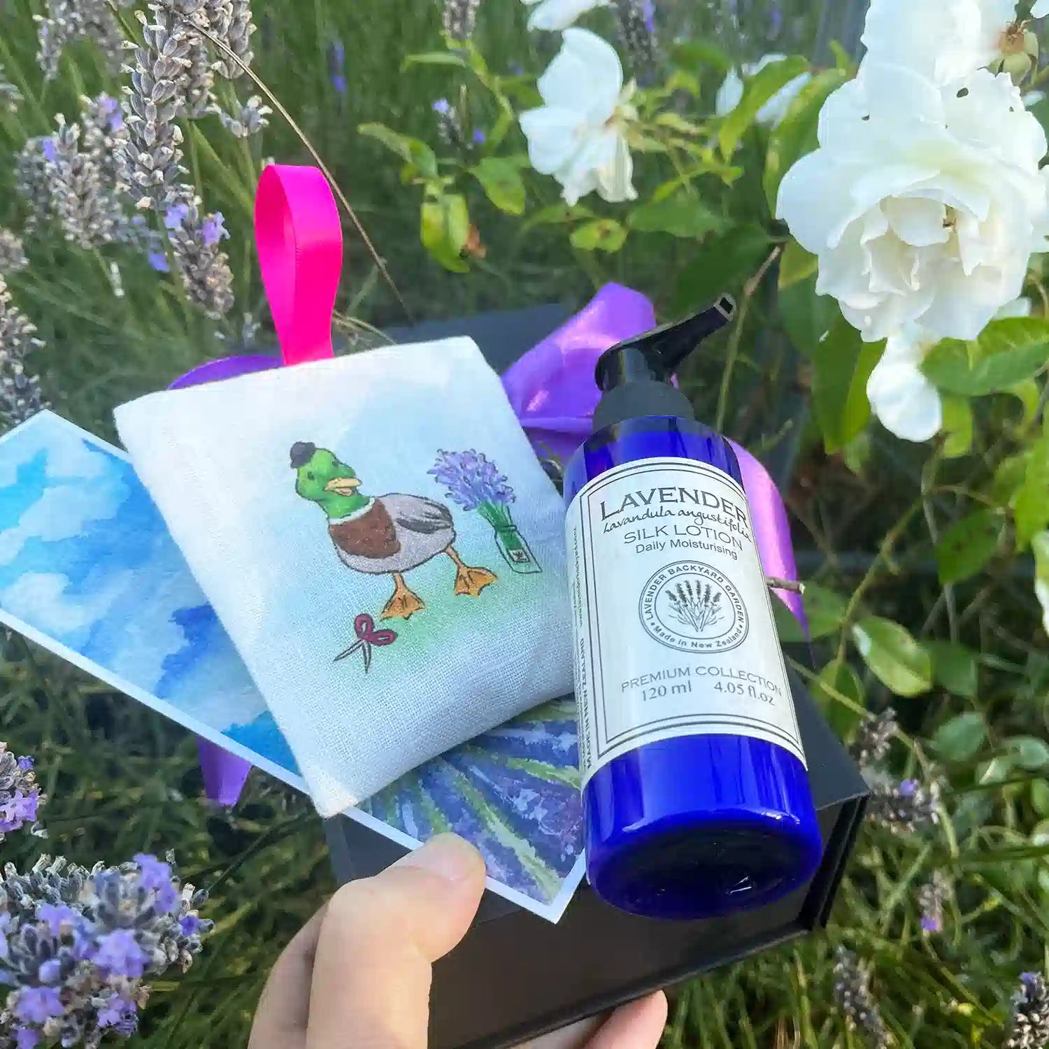 Lavender Dreams: Good Birthday Presents for Girls, featuring a beautiful gift set with Linen Lavender Scented Hanging Sachets-Duck, Moisturizing Lavender Body Lotion, Lavender Field Bookmark, and Mini Lavender Dried Flowers, set against a sunset lavender field and white roses at Lavender Backyard Garden, NZ.