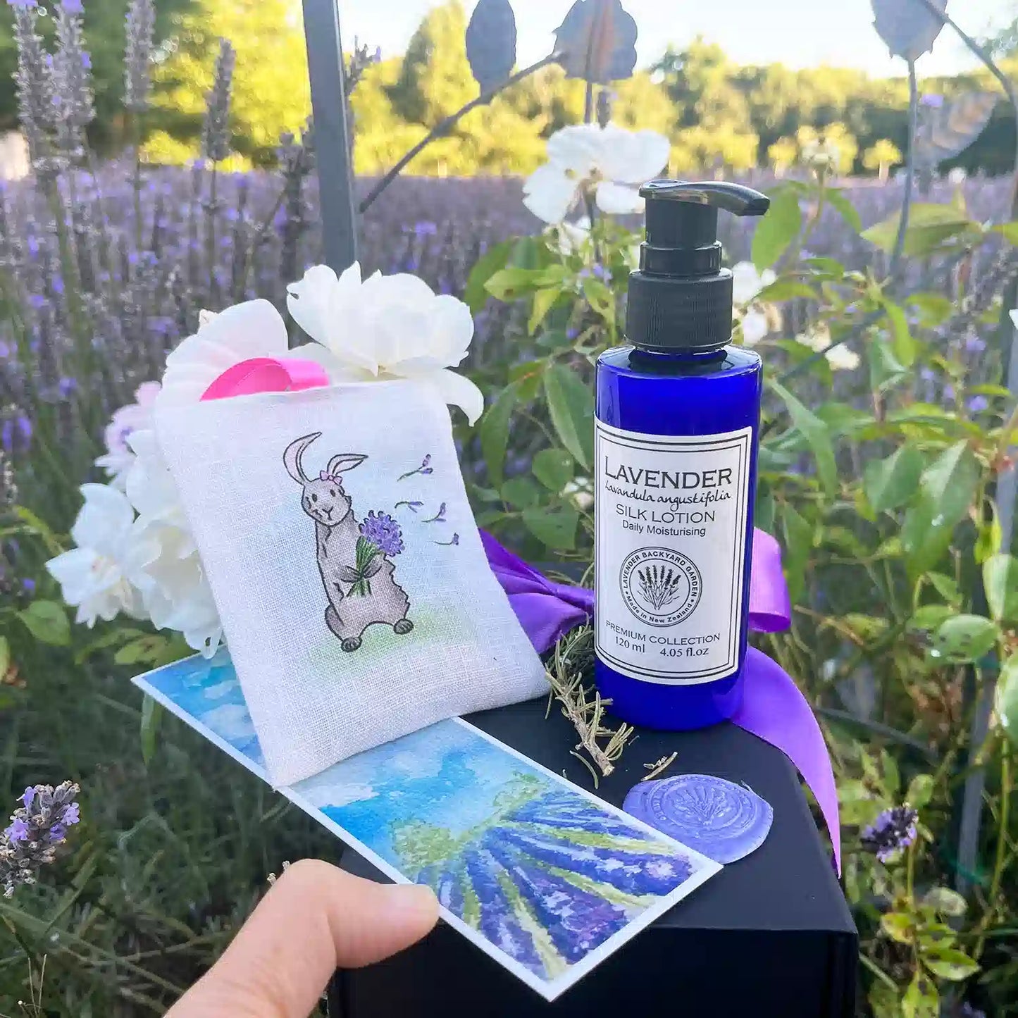 Lavender Dreams: Good Birthday Presents for Girls, featuring a beautiful gift set with Linen Lavender Scented Hanging Sachets (Rabbit), Moisturizing Lavender Body Lotion, Lavender Field Bookmark, and Mini Lavender Dried Flowers, set against a sunset lavender field and white roses at Lavender Backyard Garden, NZ.