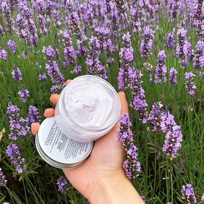 Close-up of a sugar scrub scented with lavender essential oil, with a background of fresh lavender fields in bloom.