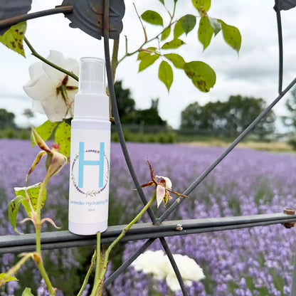 A travel-sized bottle of lavender flower water placed on a rose trill, set against the backdrop of a full-bloom lavender field in New Zealand.