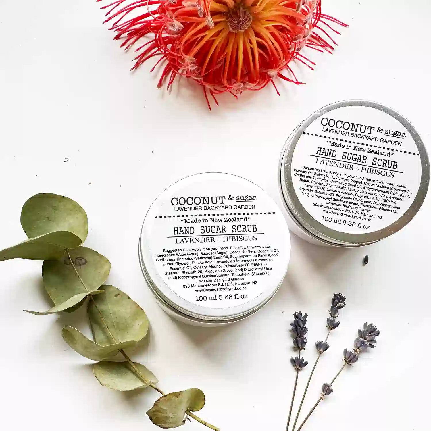 Close-up of Lavender Hand Sugar Scrub with Coconut Oil and Hibiscus, set against a background decorated with dried eucalyptus and lavender flowers.