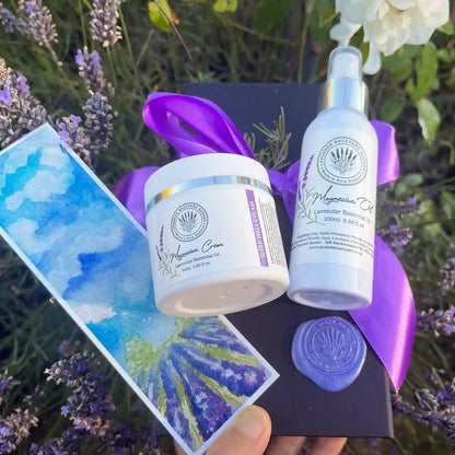 Lavender Magnesium Women's Gift Sets displayed against a sunset lavender field at Lavender Backyard Garden, featuring Lavender Magnesium Oil Sprays, Lavender Magnesium Sleep Cream, and a lavender field bookmark.