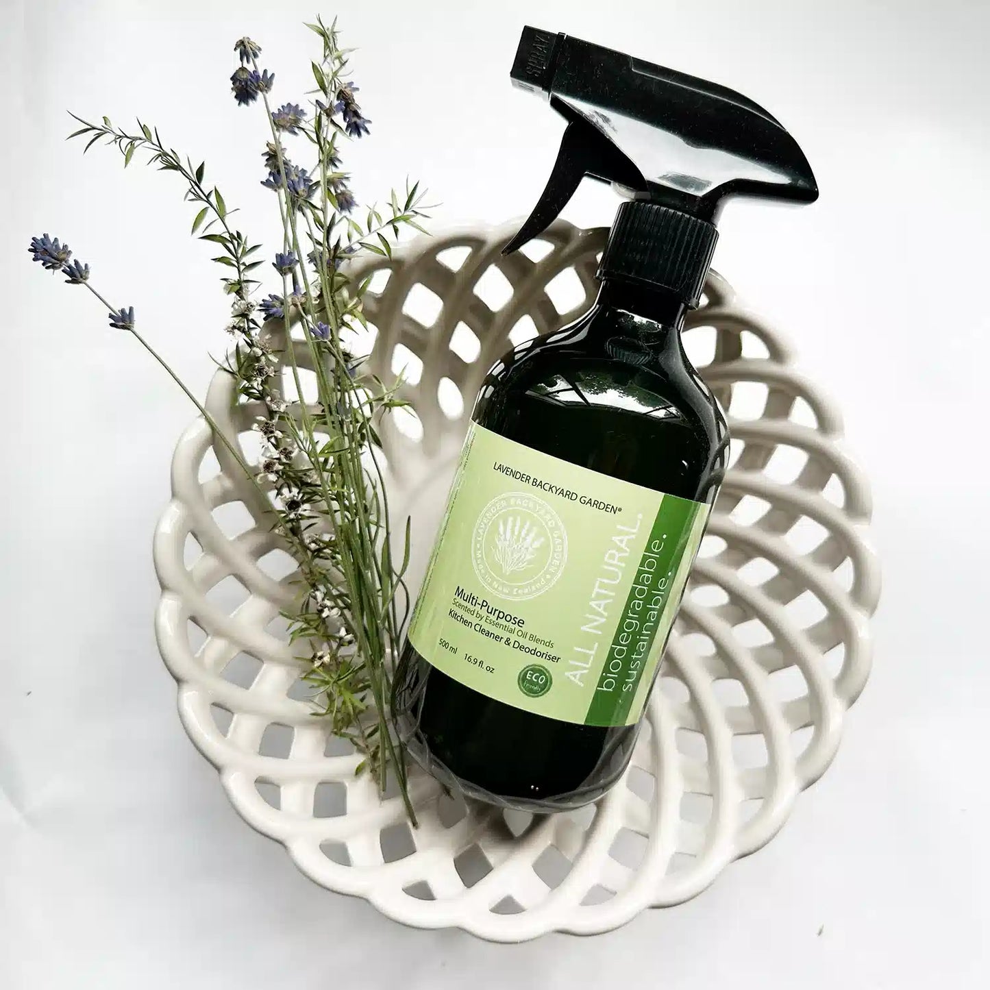 A bottle of Lavender Multi-Purpose Kitchen Cleaner placed on a decorative plate with Manuka tea tree leaves and English lavender flowers.