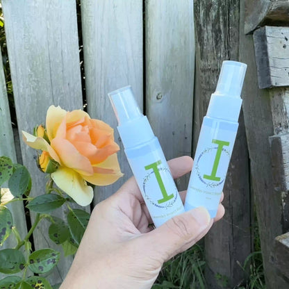 Two bottles of insect repellent spray held by hand against a wooden fence adorned with roses.