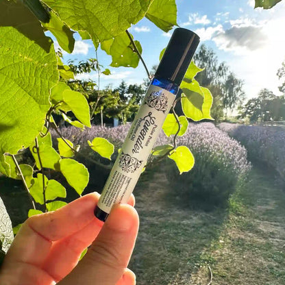 Lavender Natural Perfume Pulse Point Roll On, with a background of kiwi fruit vine and rows of lavender blooming at Lavender Backyard Garden, New Zealand.