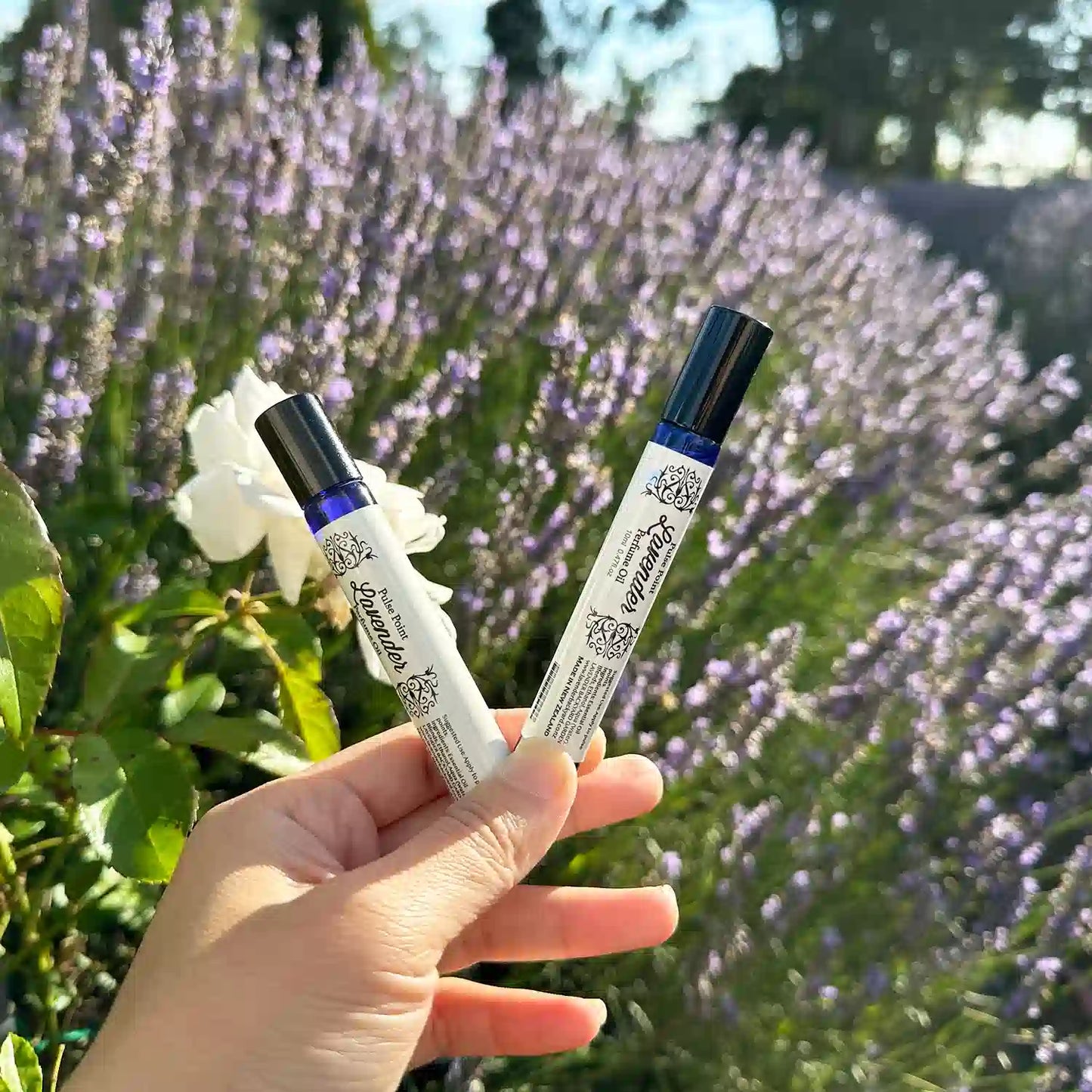 Two Lavender Natural Perfume Roller Blends, held by hand against a purple blooming lavender field at Lavender Backyard Garden, New Zealand.