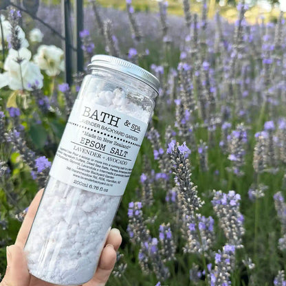 Lavender Relaxing Epsom Bath Salt holding by hand against purple blooming lavender and white roses.