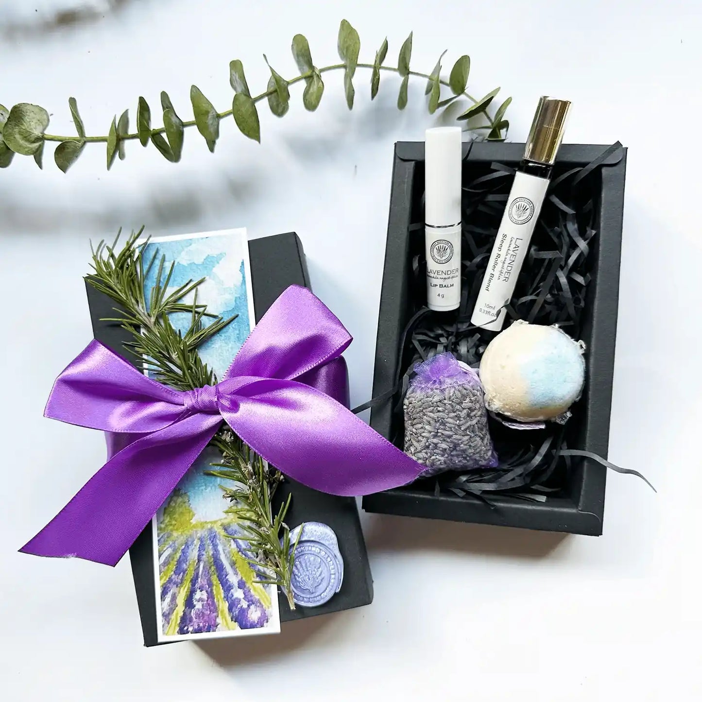 Lavender Restoration Ritual Gift Set featuring lavender sleep roller blend, lip balm, bath bomb, and lavender sachet, beautifully wrapped with a purple ribbon, dried rosemary, and a lavender field bookmark.