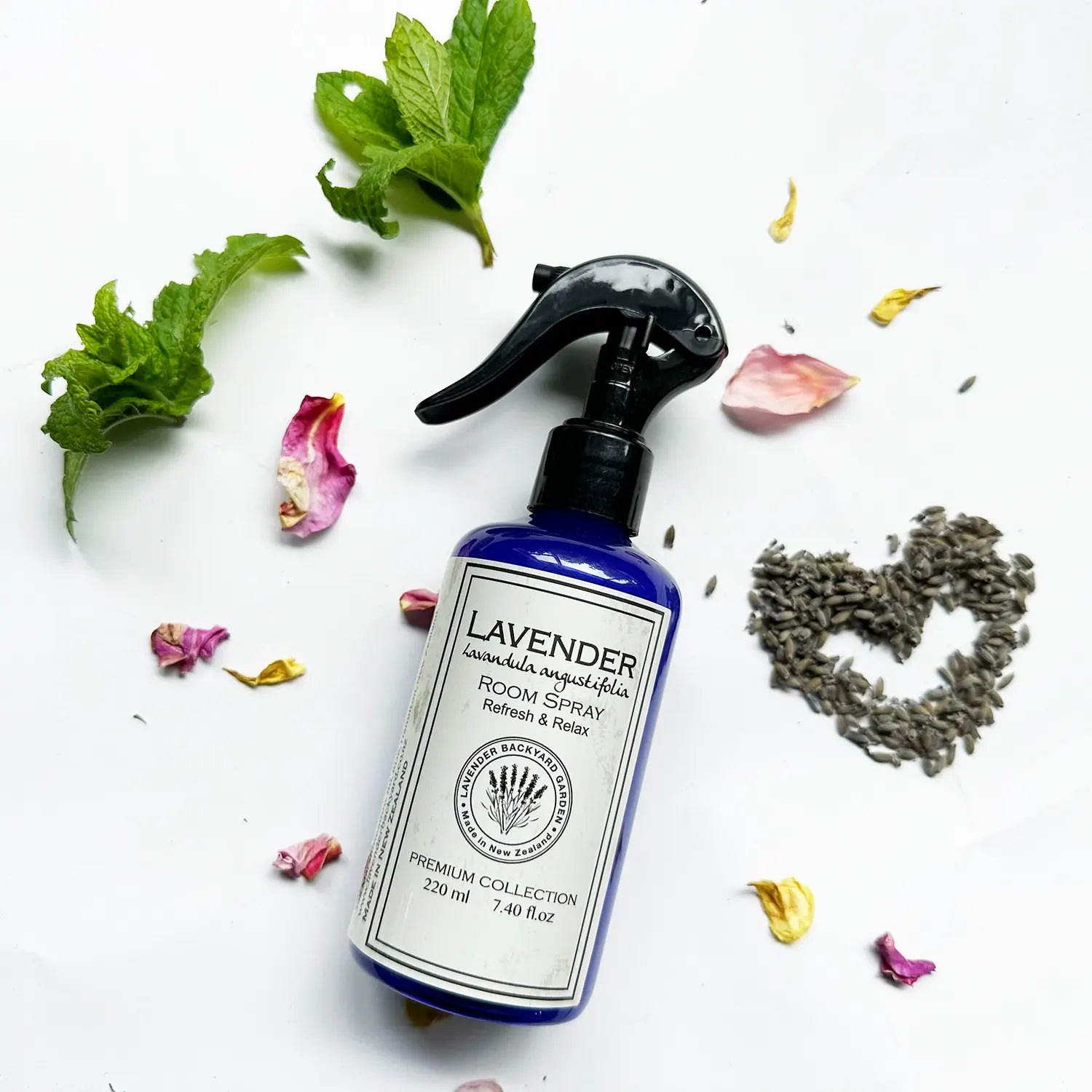 Lavender Room Freshener Spray for Home with background decor of fresh mint leaves, rose petals, and dried lavender flower buds.