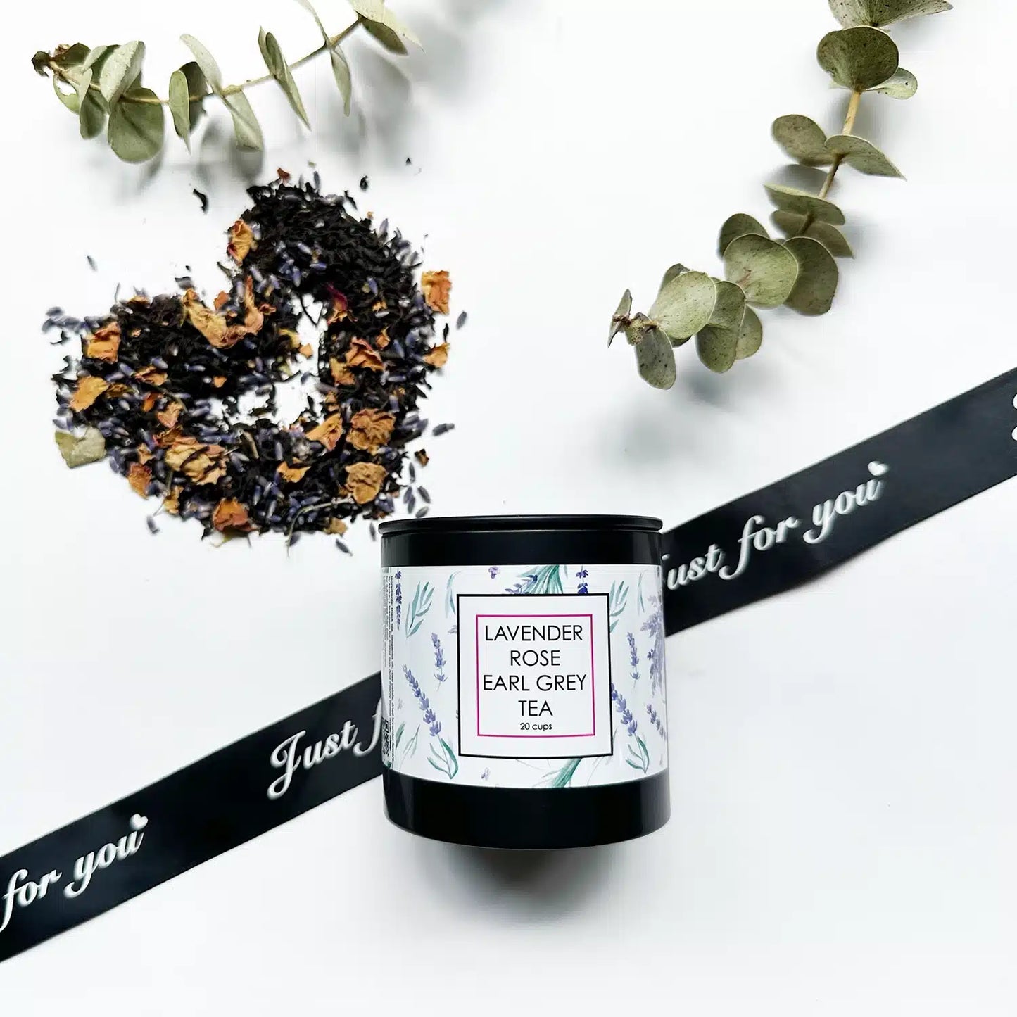 Lavender & Rose Earl Grey Tea - Loose Leaf, with tea leaves and herbs displayed in the background, accented by a black ribbon and eucalyptus leaves.