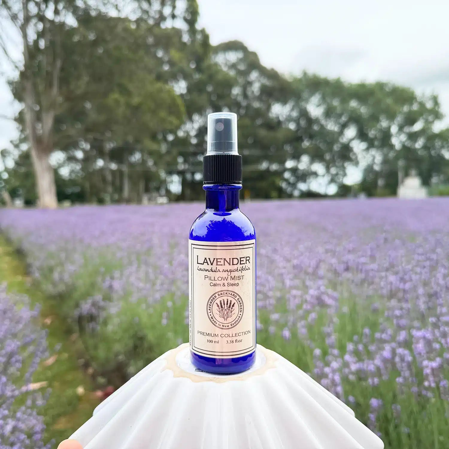  A bottle of lavender sleep spray placed on a plate, set against the background of a vibrant lavender field in full bloom at Lavender Backyard Garden in New Zealand.