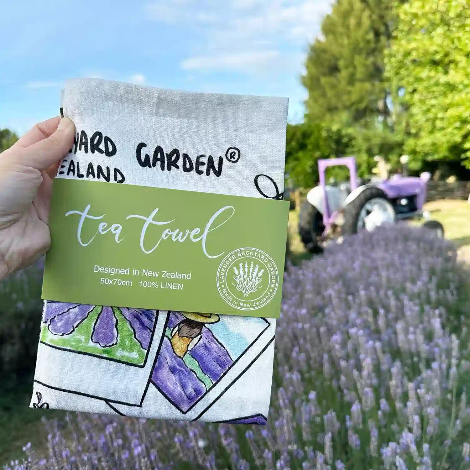 Folded Linen Tea Towel - Memory of Lavender Farm with a green package banner against purple tractors, lavender bloomings at Lavender Backyard Garden.