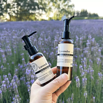 Luxury lavender bath oils held by hand against a sunset backdrop of lavender fields at Lavender Backyard Garden, NZ.